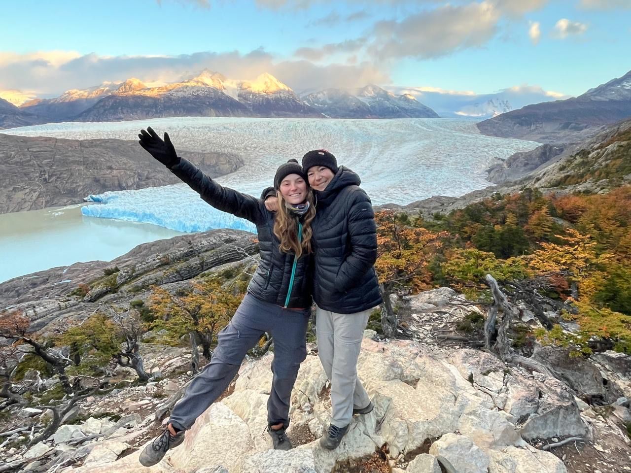Two friends embracing on a rocky overlook above Glacier Grey, golden evening light on the surrounding peaks