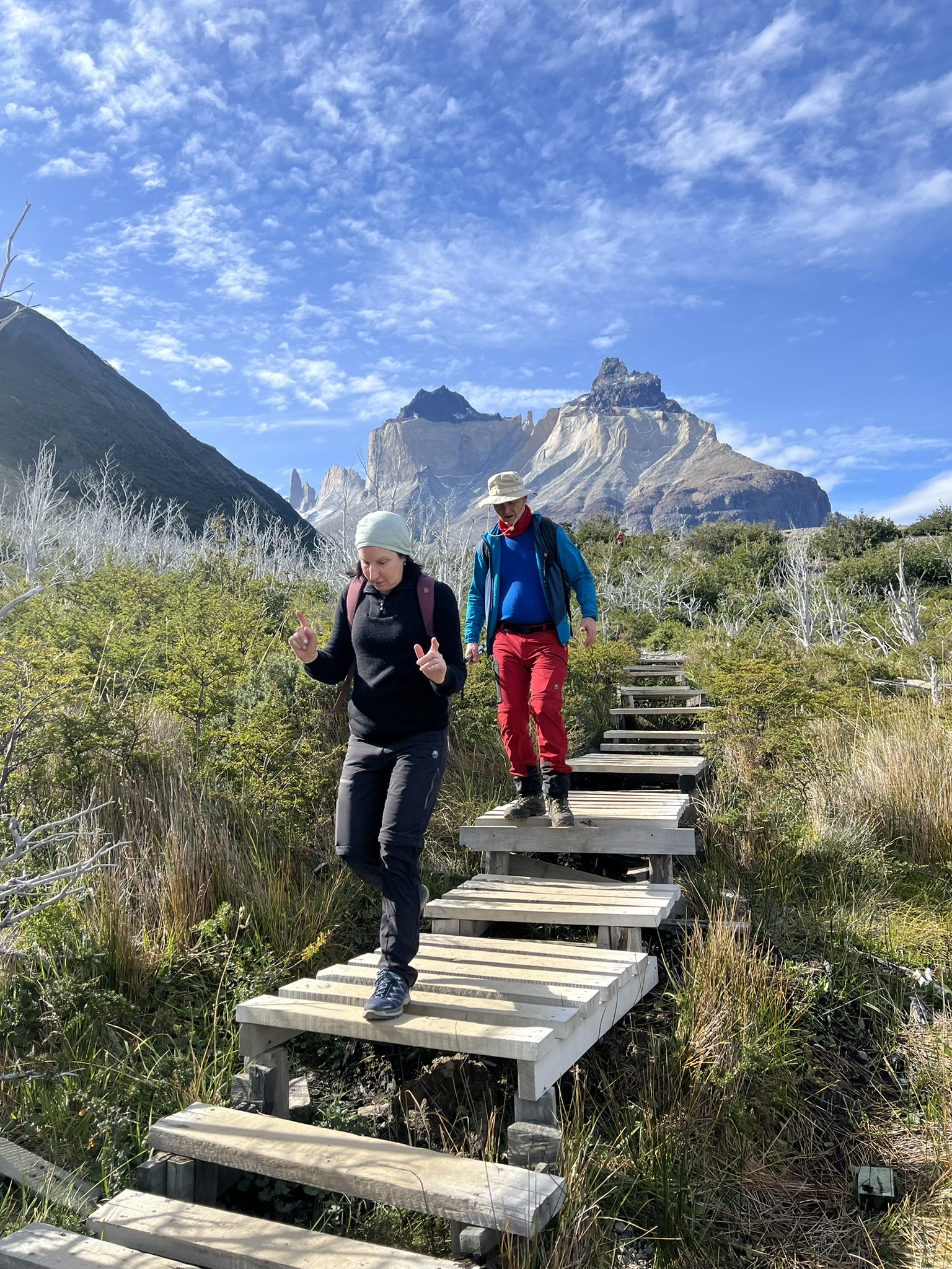 Two hikers descending a wooden boardwalk trail with the Cuernos del Paine peaks behind them
