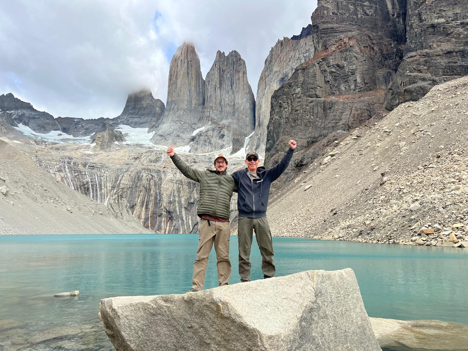 Two friends celebrating with arms raised at the base of the Torres del Paine towers